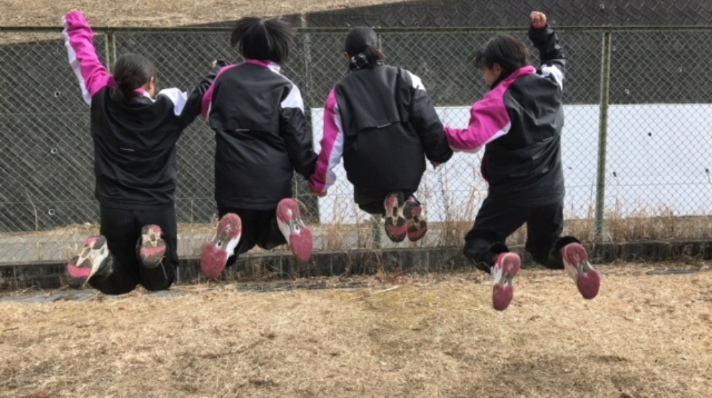 中学生の陸上部の仲間が一緒にジャンプしている後ろ姿
